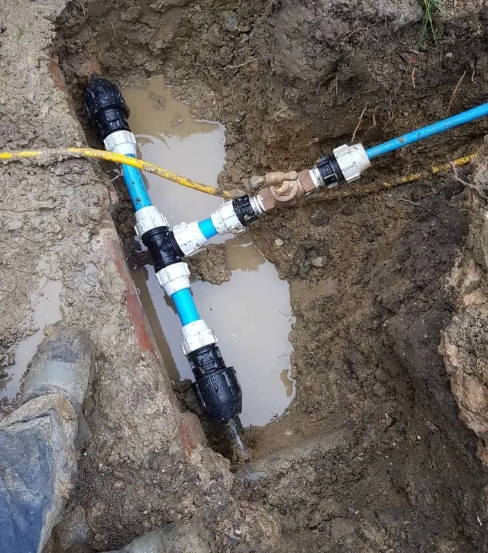 Blue MDPE water supply pipe with compression fittings and a tee connection in an excavation